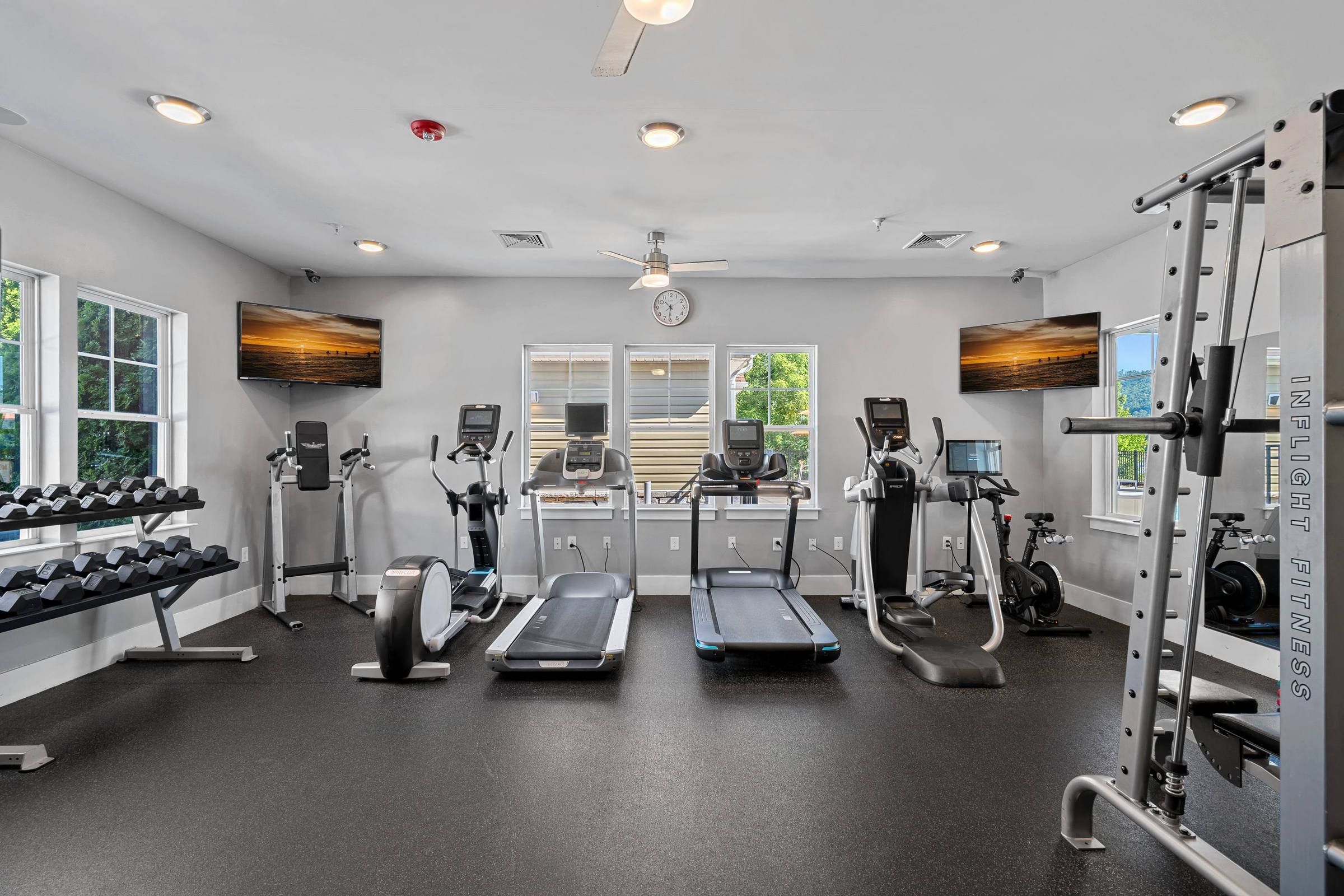 Bright gym room with treadmills, dumbbells, elliptical machines, stationary bikes, and a multi-function workout station.